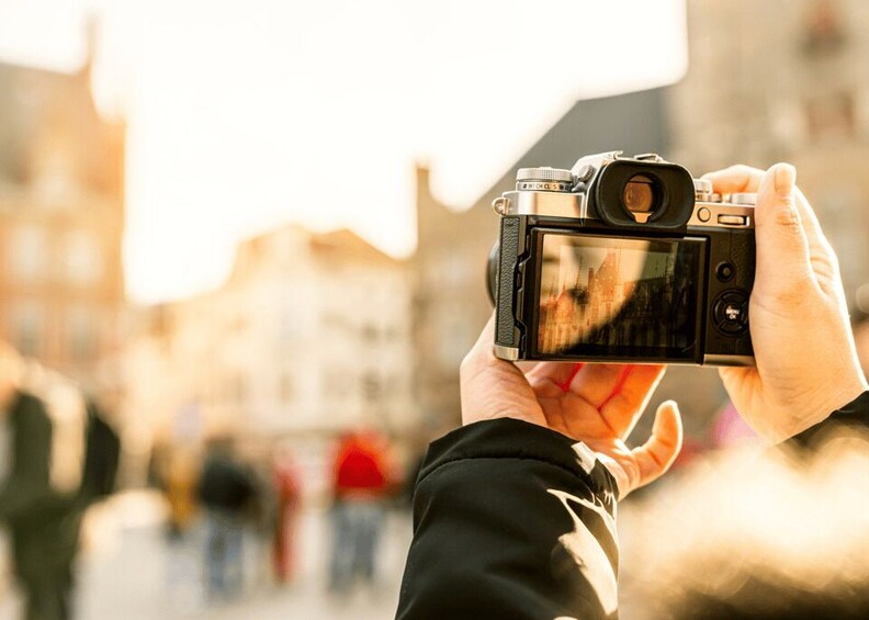 A person holding a camera with a viewfinder, capturing a scene with buildings in the background. 1