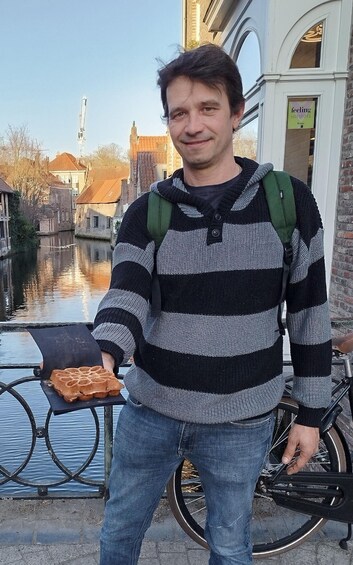 Henkilö, jolla on vohveli kädessään, seisoo kanavan varrella. Taustalla näkyy rakennuksia ja polkupyörä. 2
