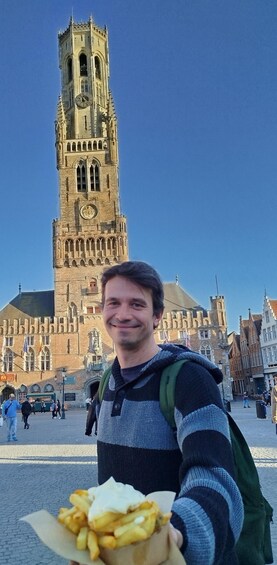 Henkilö, jolla on kädessään kori ranskalaisia, seisoo historiallisessa tornissa, jossa on kello. 1