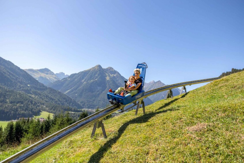 A person seated on a blue chairlift moving along a metal track through a mountainous landscape. 1