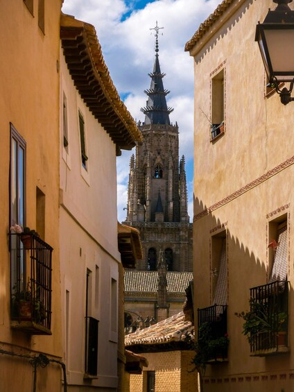 A narrow street between buildings with a church tower in the background. 4
