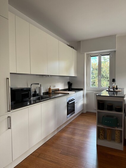 A modern kitchen with white cabinets, a black countertop, and a window with a view of greenery. 4