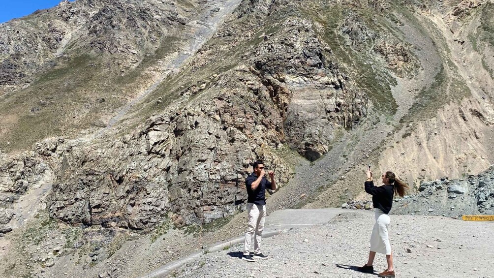 Two people taking photos in a rocky mountainous area with a dirt path. 2