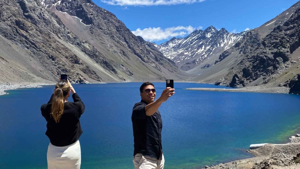 Two people taking a selfie with a mountain lake and snow-capped peaks in the background. 1