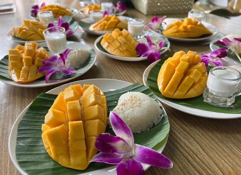 A table with plates of mango dishes, including mango salad and mango sticky rice, garnished with purple flowers. 4
