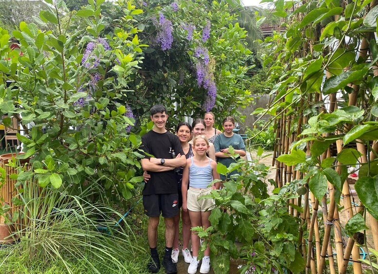 A group of people standing in a garden with lush greenery and purple flowers. 2