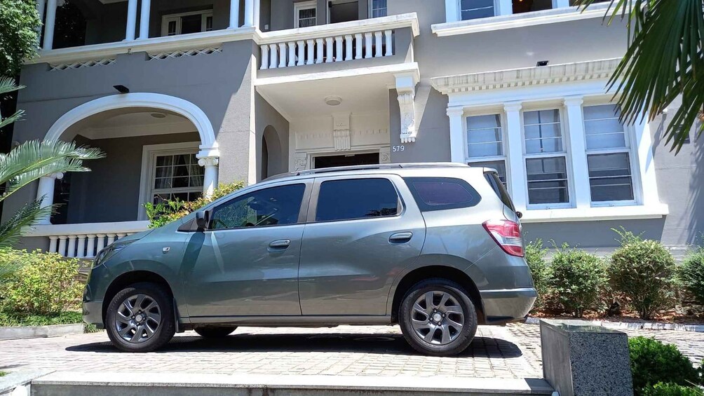 A silver SUV parked in front of a gray two-story house with a balcony. 2