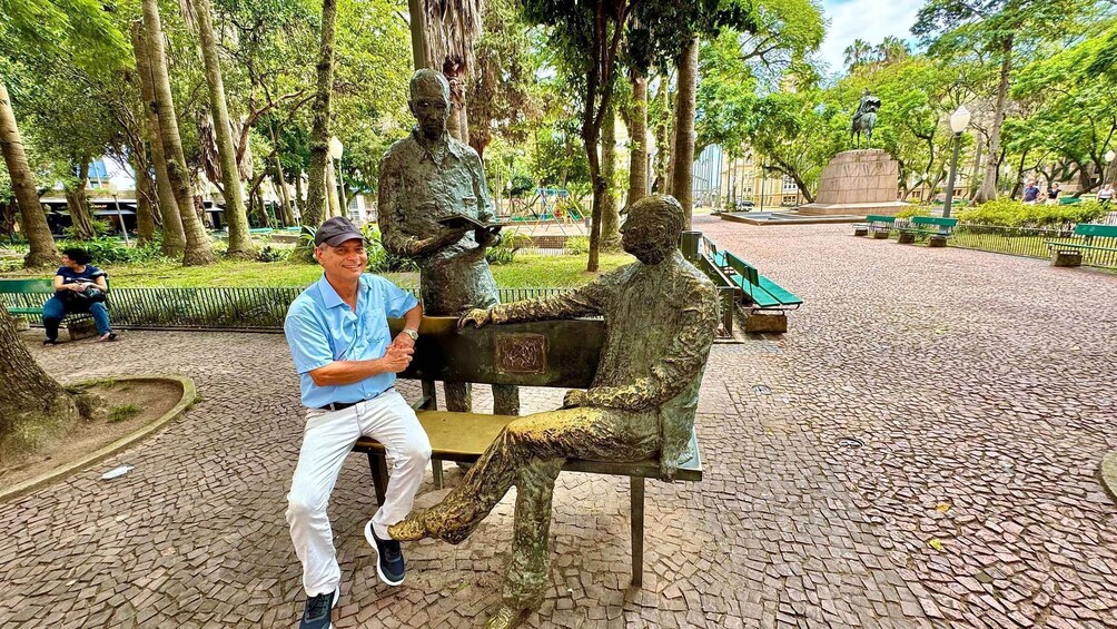 A man sitting on a bench next to a statue of a man playing a guitar. 3