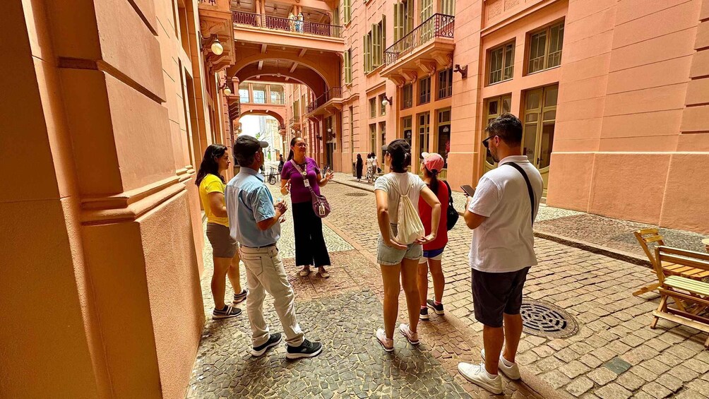 A group of people standing on a cobblestone street in a historic area with pastel-colored buildings and a covered passageway. 4