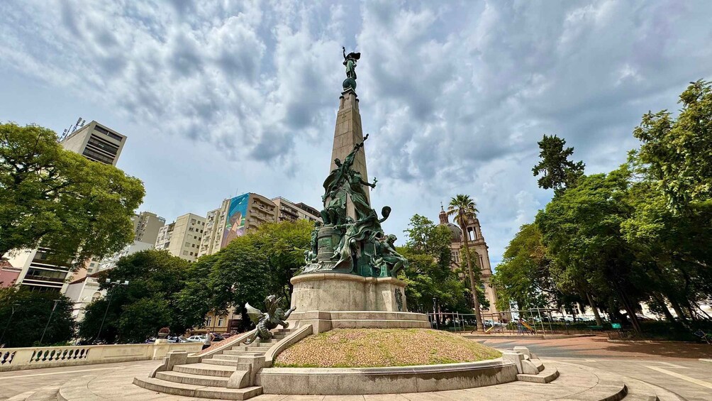 A statue in a park with steps leading up to it, surrounded by trees and buildings. 5