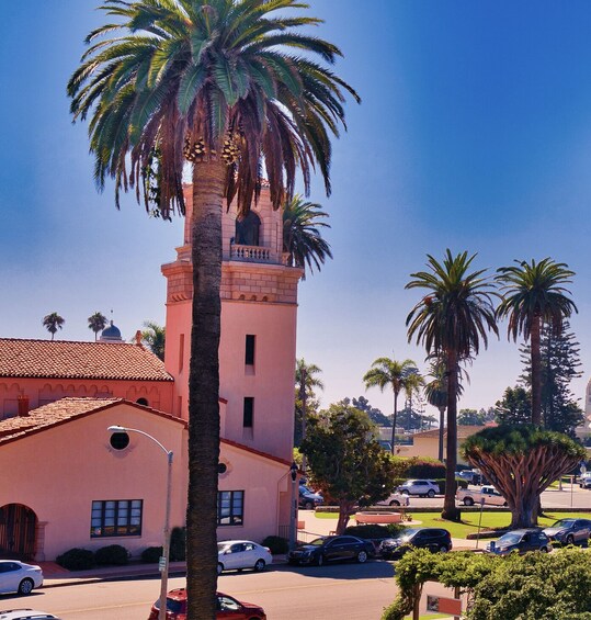 A pink building with a tower, palm trees, and parked cars. 3