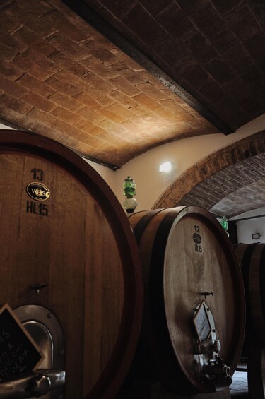 Wooden wine barrels with numbers and a metal valve in a dimly lit cellar. 4