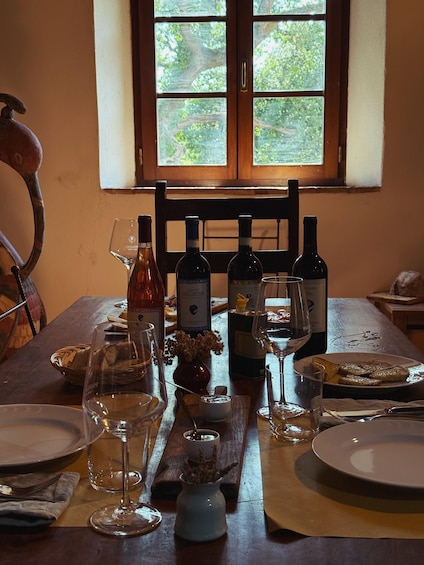 A dining table set with wine bottles, glasses, bread, and a vase with dried flowers. 2