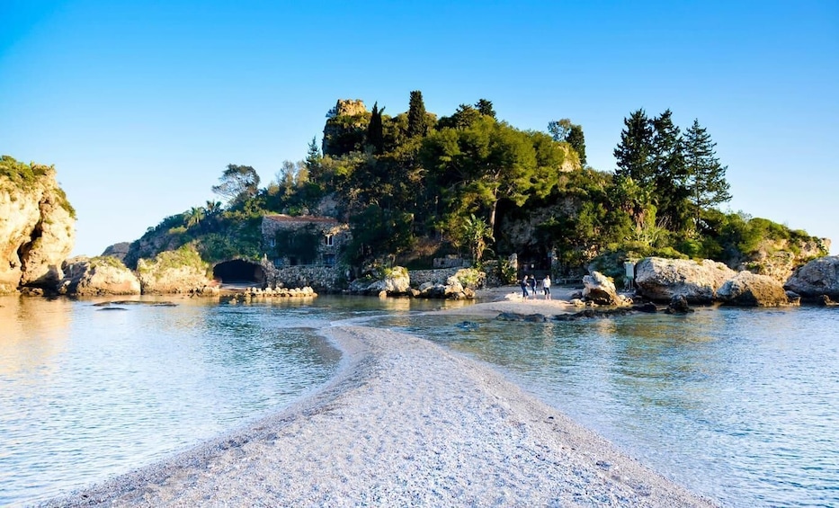 A pebble beach leading to a rocky island with a cave entrance and lush greenery. 1