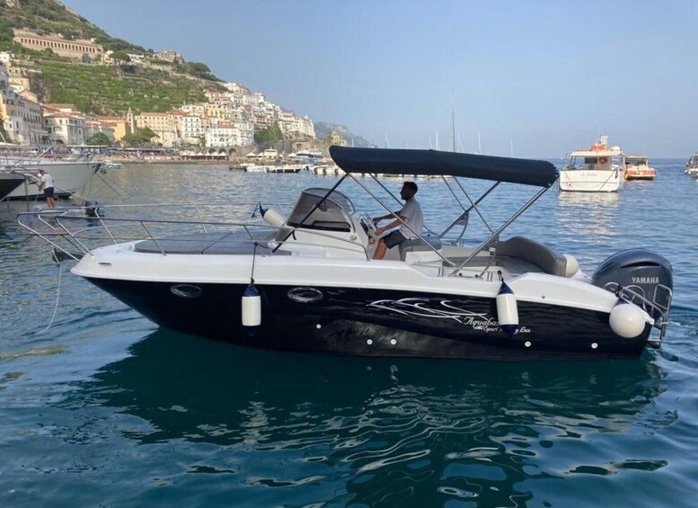 A black and white motorboat with a Yamaha engine on calm water, docked near a coastal town with buildings on a hillside. 3