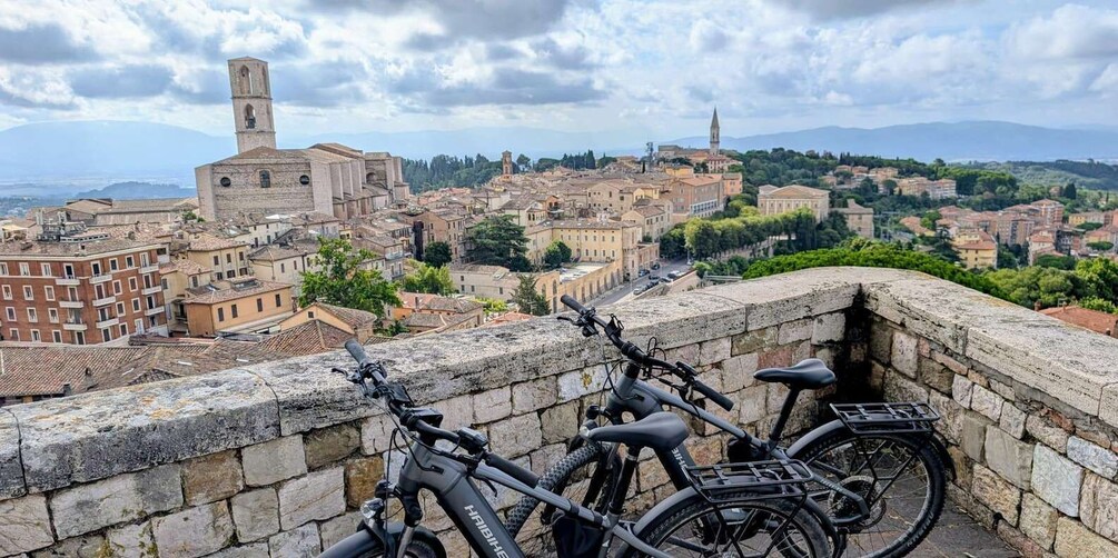 A historic cityscape with stone buildings, a prominent tower, and bicycles parked on a stone wall. 1