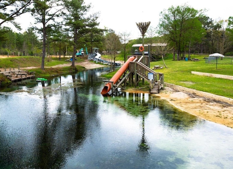 A water slide structure extending over a calm river, surrounded by trees and picnic areas. 3