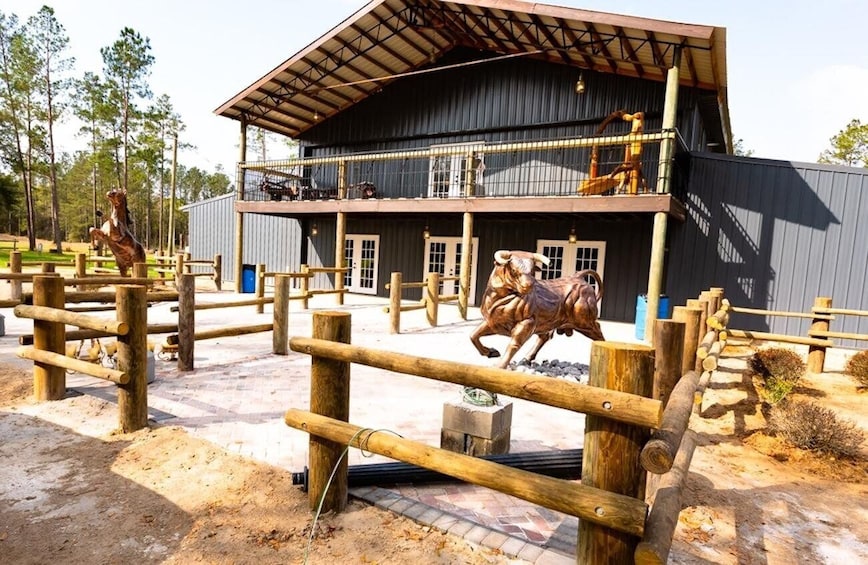 A stable with a wooden fence, a horse statue, and a building with a balcony. 4