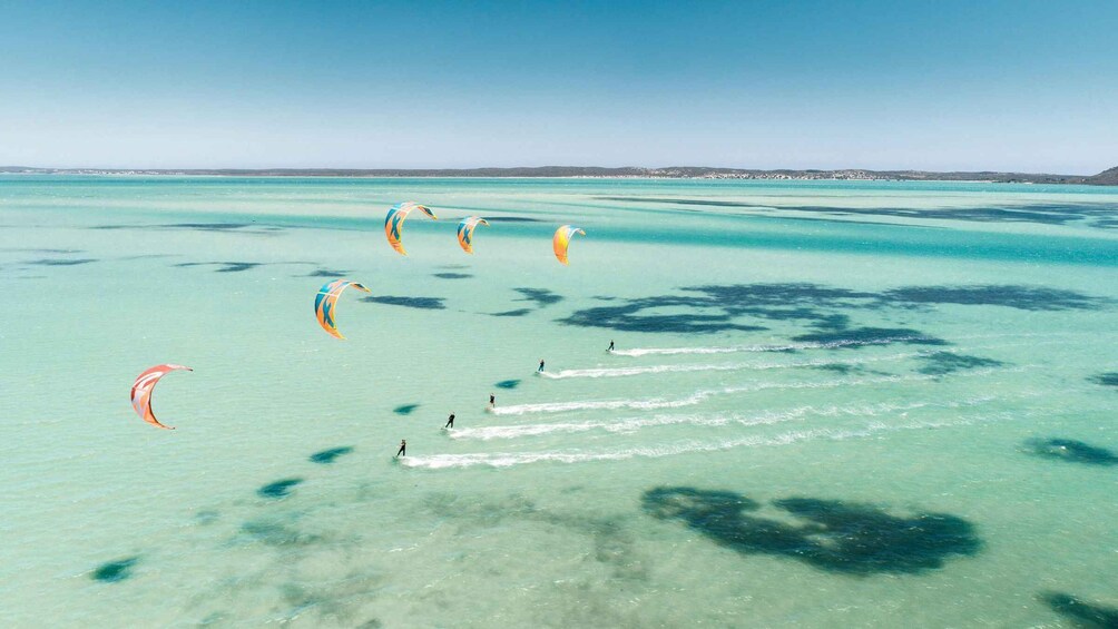 A clear turquoise sea with several people windsurfing and kitesurfing. 1