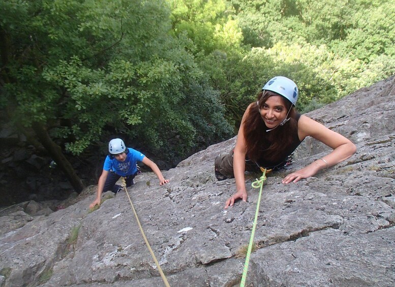 Two people climbing a rocky slope in a forested area. 5