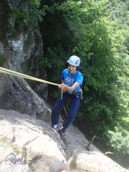 A person rappelling down a rocky cliff with a rope, surrounded by dense green foliage. 4