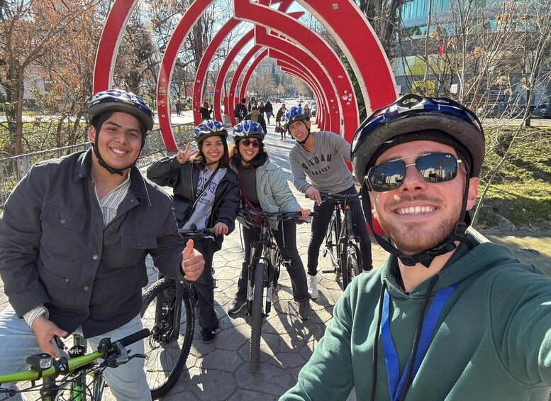 A group of cyclists on a paved path with a large red circular structure in the background. 4
