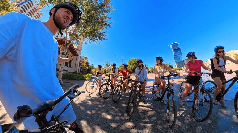 A group of cyclists on a sunny day, with buildings and trees in the background. 5