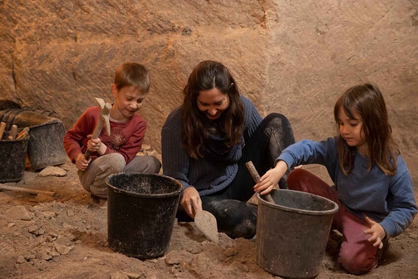 Three individuals engaged in an outdoor activity, possibly related to excavation or construction, with tools and buckets on the ground. 3