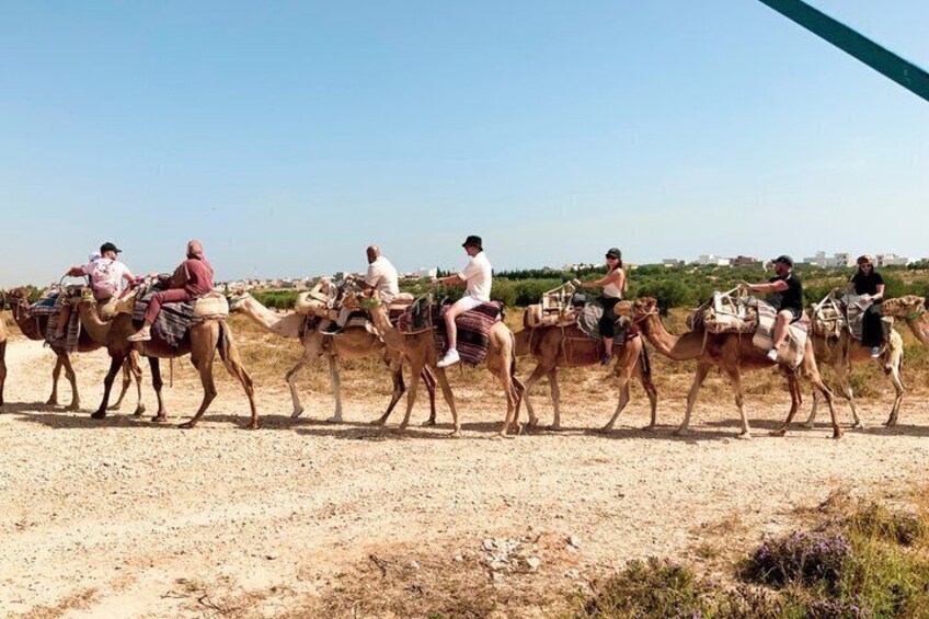 A group of people riding camels on a dirt road in a desert landscape. 4