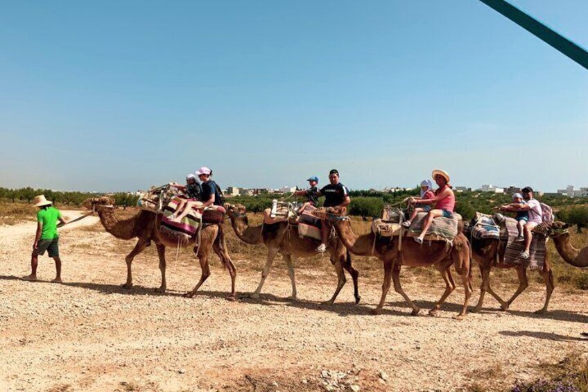 A group of people riding camels on a dirt path with a clear sky. 1
