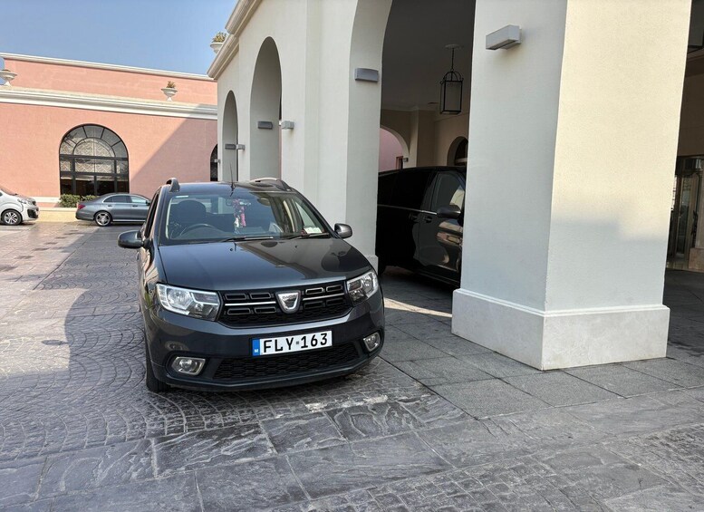 A black car parked in a driveway with a white building in the background. 3