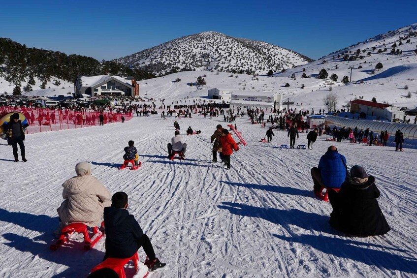 A snowy ski slope with people sledding and a mountain in the background. 2