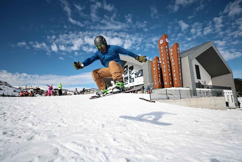 A snowboarder performing a jump in a snowy area with a building and a clear sky in the background. 1
