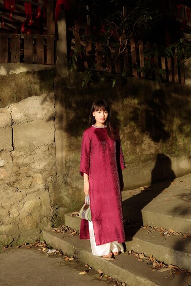 A person standing on stone steps with a red dress, a wooden fence, and a tree in the background. 3