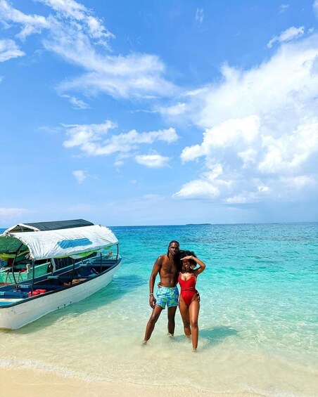 A couple standing on a beach with a boat in the water. 2