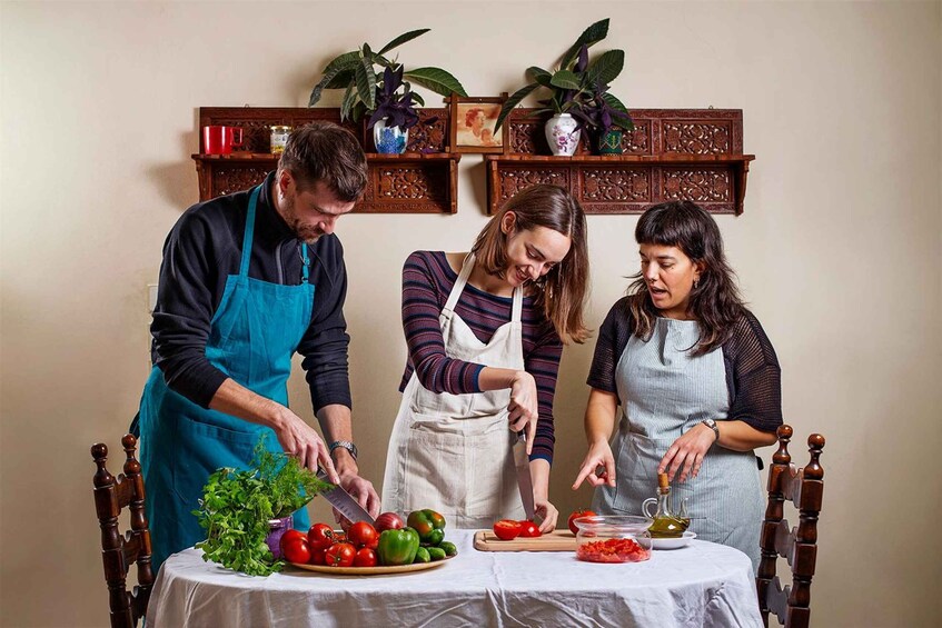 Three people preparing food with vegetables and a cutting board on a table. 1