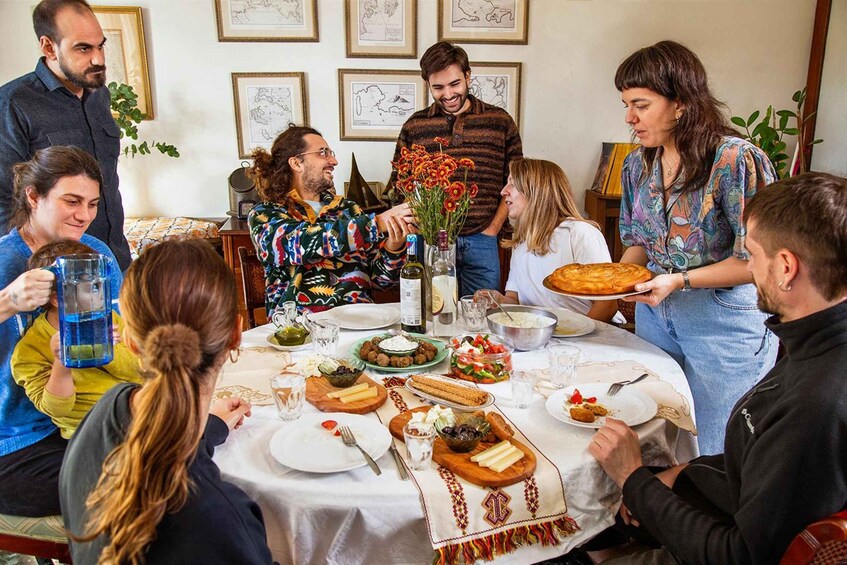 A group of people around a table with food, drinks, and a bottle of wine. 4