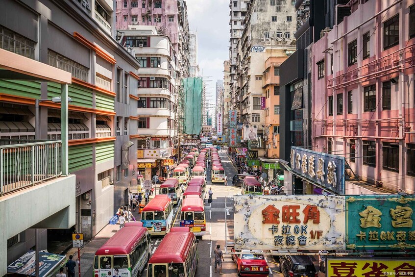 A busy urban street with multiple buses and cars, surrounded by multi-story buildings with various signs and advertisements. 4