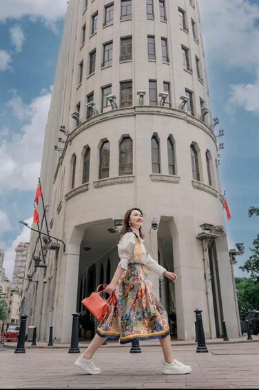 A person walking in front of a tall, white building with arched windows and air conditioning units. 1