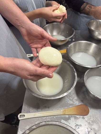 A person holding a round dough over a bowl of liquid, with other bowls and a wooden spoon visible. 5