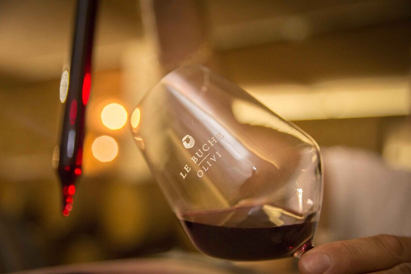 A hand holding a wine glass with 'LE BUCHER OLIVI' etched on it, filled with red wine. 3