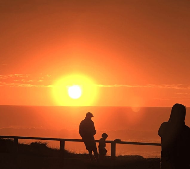 A sunset over a body of water with silhouettes of people and a railing. 2