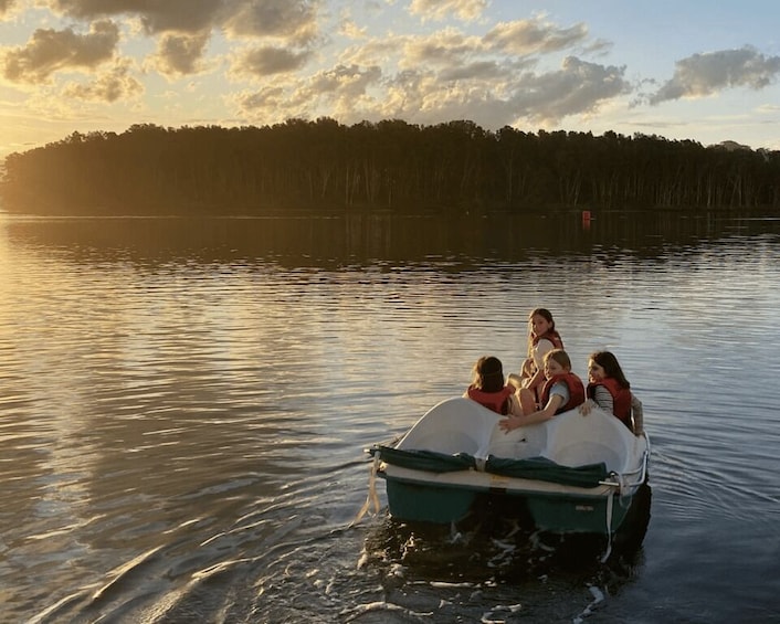 A group of people on a small boat on calm water with a forested shoreline in the background. 1