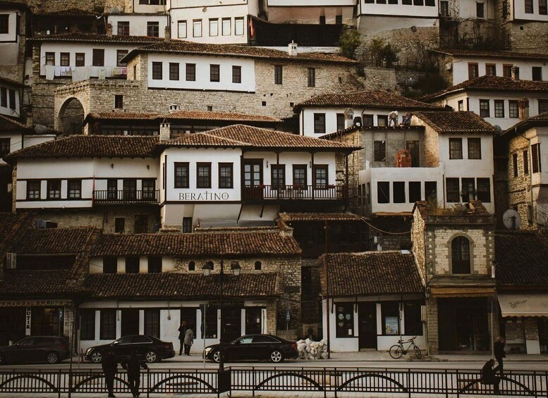 A historic town with multi-story buildings, a visible shop named 'BERATINO,' and a street with cars and pedestrians. 1