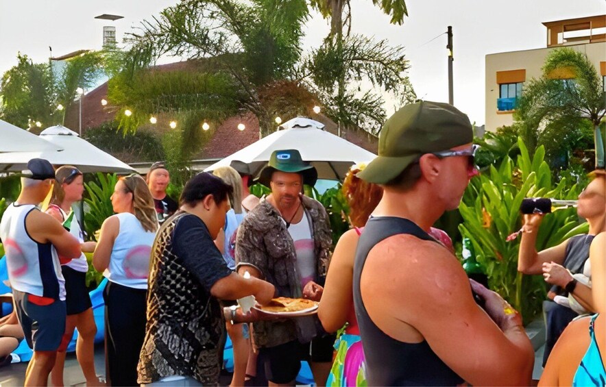 A group of people outdoors, some holding plates of food, under umbrellas. 2