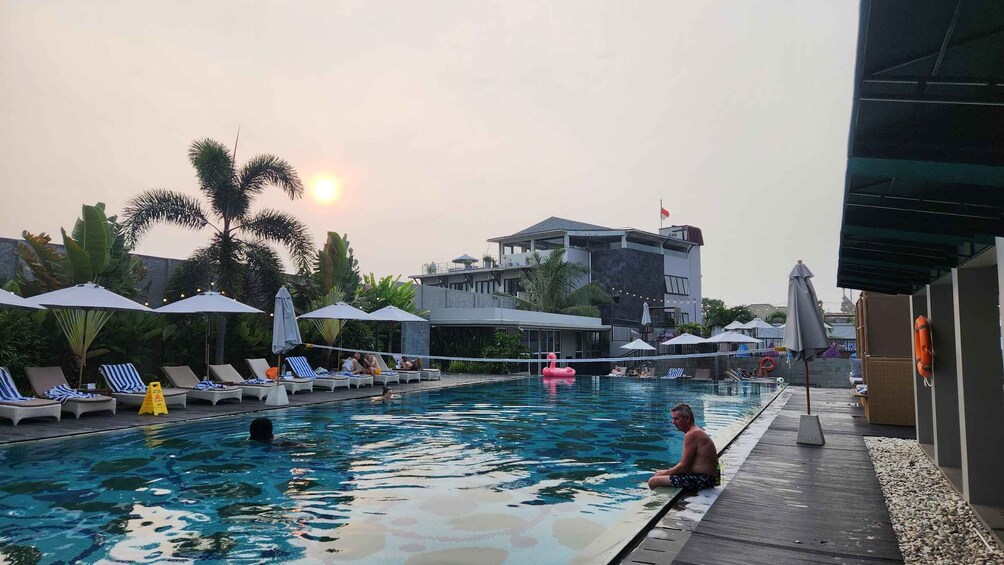 A swimming pool with lounge chairs and umbrellas, surrounded by palm trees and a building with a flag. 3
