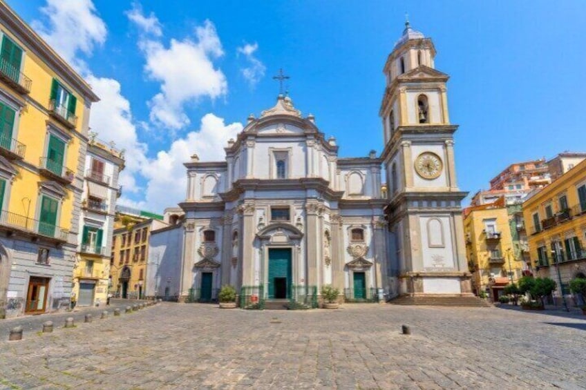 A historic church with a bell tower, cobblestone street, and surrounding buildings. 1