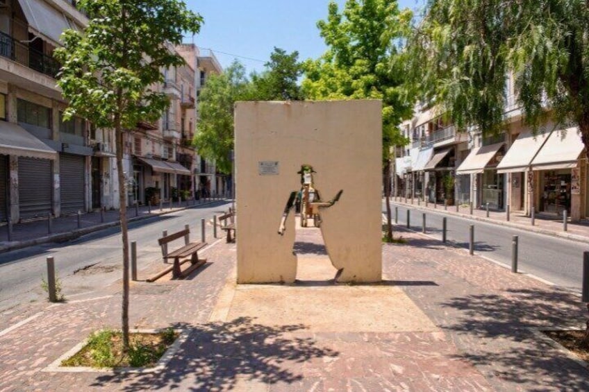A street with buildings, a sidewalk, a tree, and a bench. 2