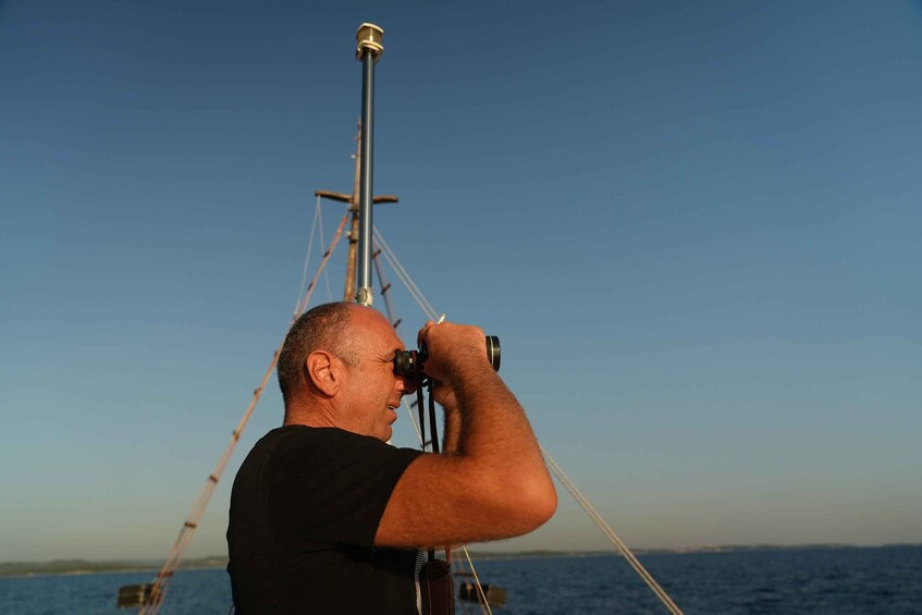 A person using binoculars on a boat with a clear sky and calm sea. 1