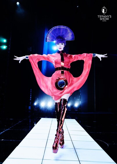 A person in a red dress with a large hat walking on a stage. 2